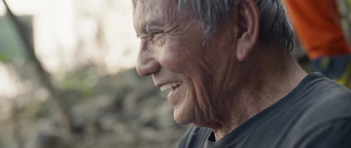Older man smiles and laughs as young boys walk near him