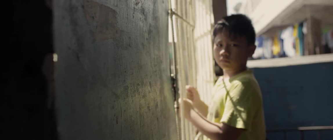 The child looks to his side holding onto a gate