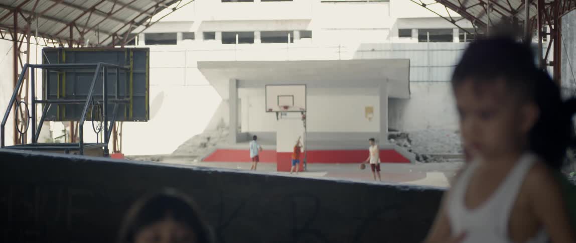 Children stand on a balcony while others play basketball below