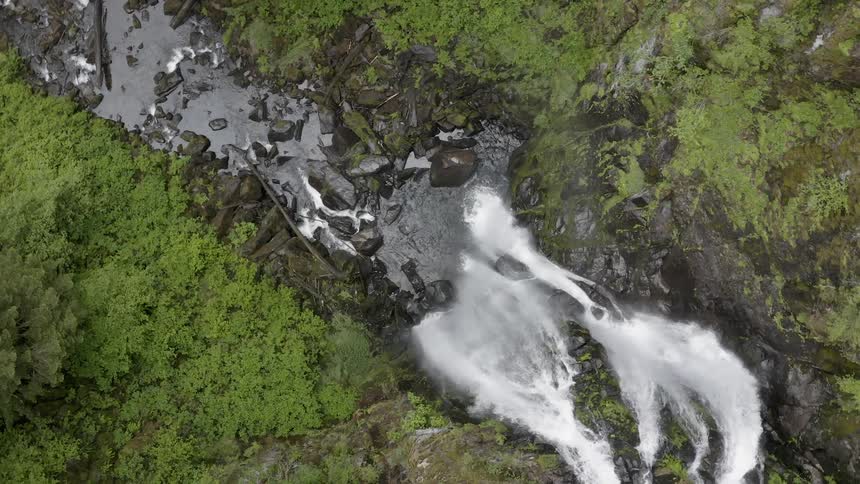 Spinning aerial shot a waterfall flowing into a rocky creek below