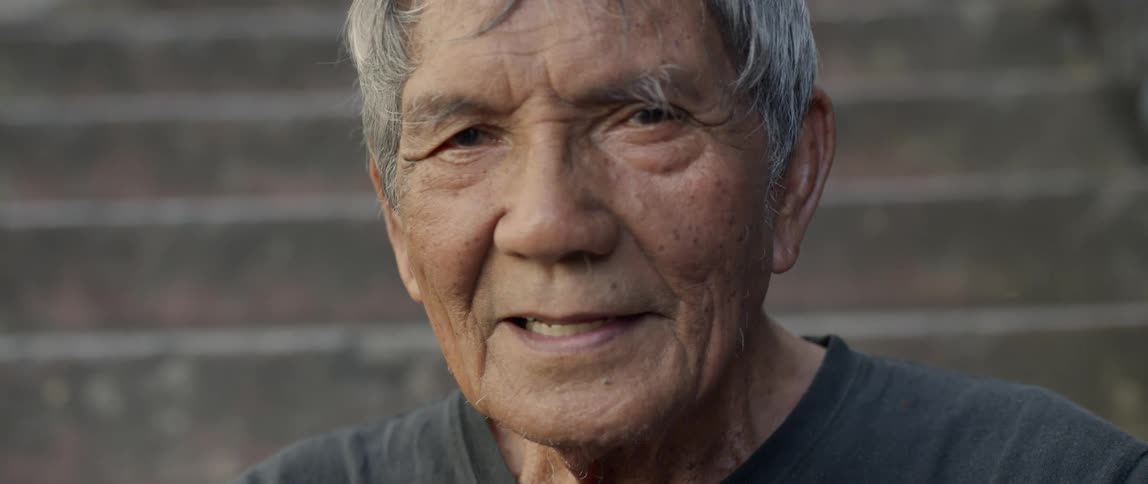 Elderly man smiles in front of a wall