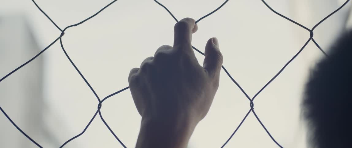 A hand is hanging on the chain link fence