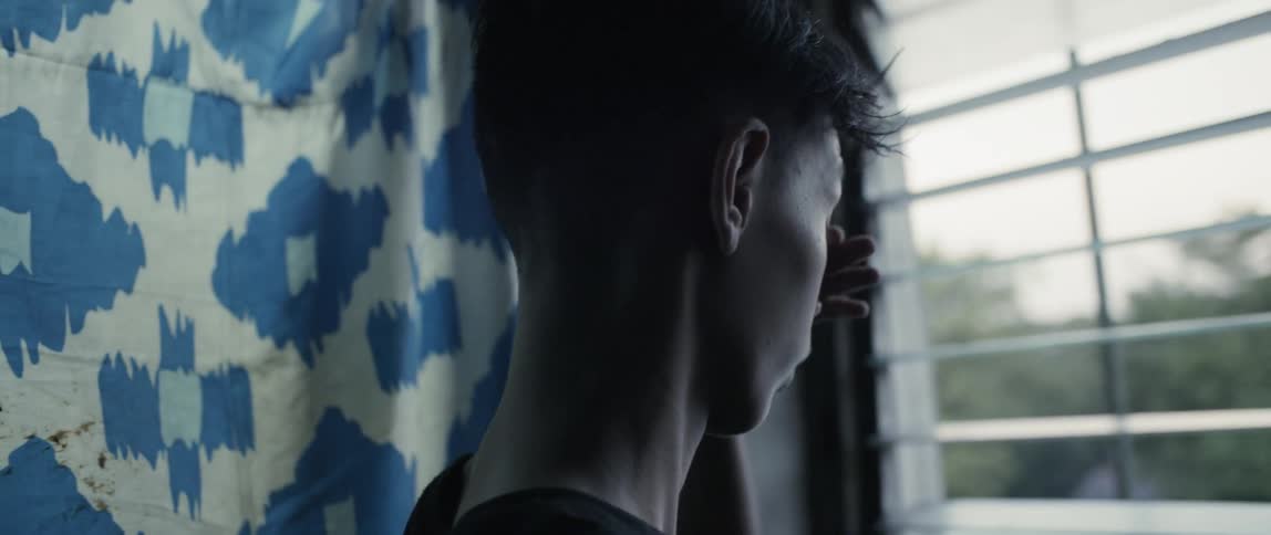 A boy rubs his eyes looking out the window