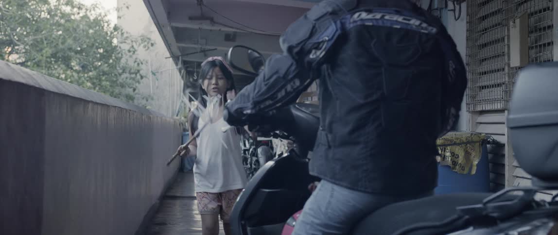 A child carries a stick towards a man on the motorcycle