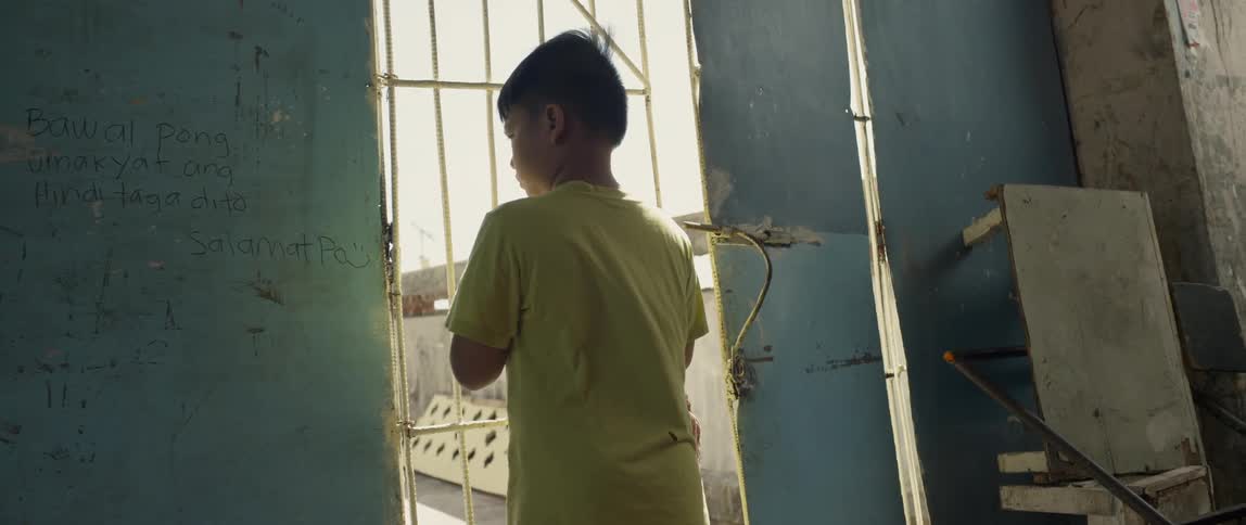 Child stands in a tumbledown building looking out the door