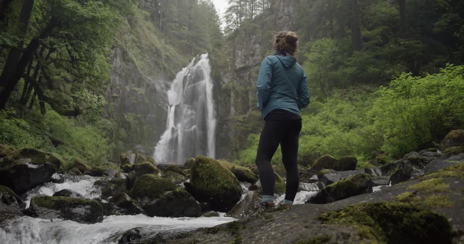 Shaky shot of a woman in a lush forest watching a cascade