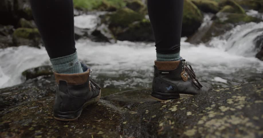 A woman stands near the edge of a creek with hiking boots on