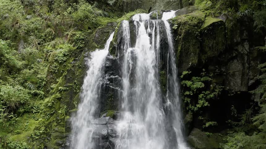 Aerial shot of a waterfall rushing over rocks in a flourishing forest 