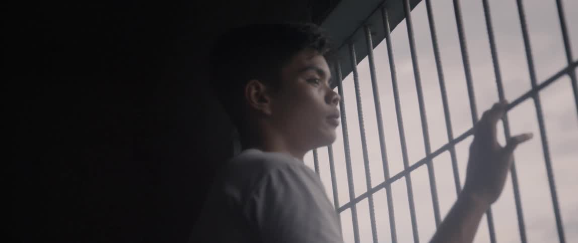 A boy looks out of a barred window