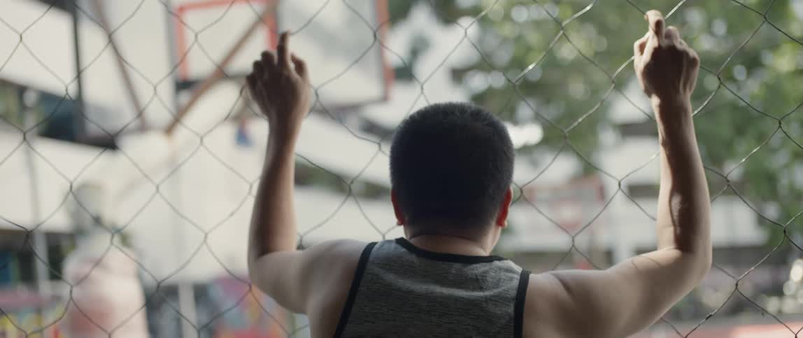 A man leans against the fence near the basketball court