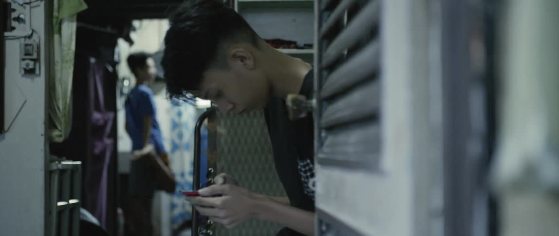 Man sits in a small room looking down at his phone