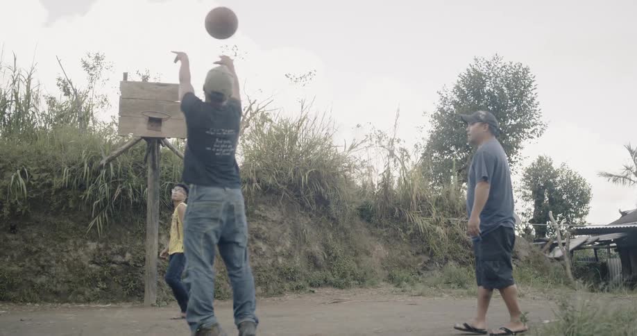 Men play basketball outside on a dirt road