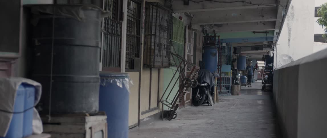 Items are stored and people walk long an apartment building open air hallway