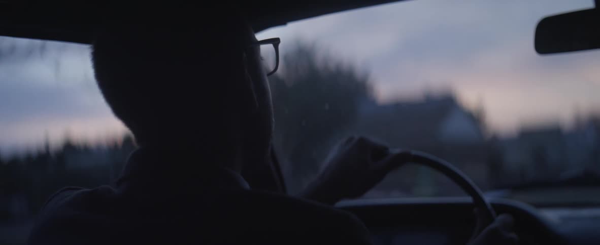 A man wearing glasses drives through a neighborhood