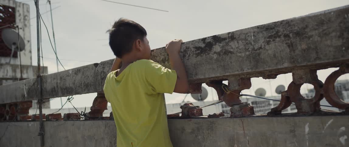 A boy reaches to look over the rooftop