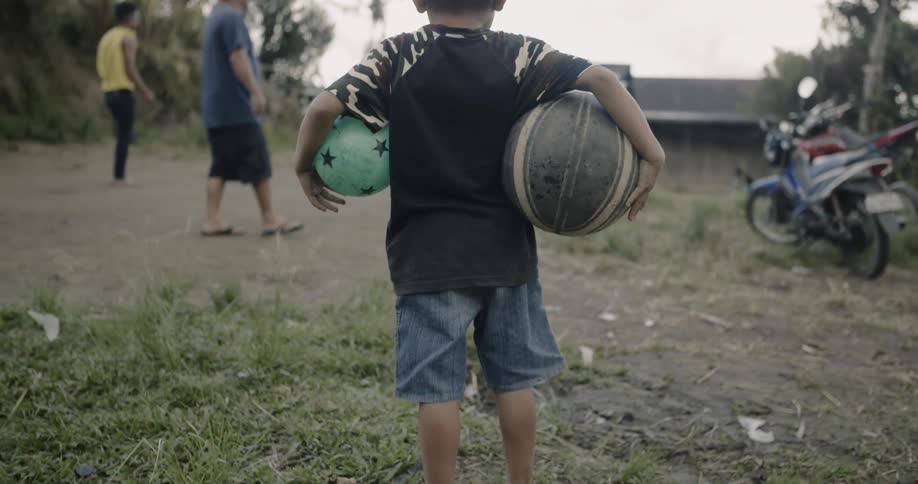 Child holds two play balls in a grassy yard