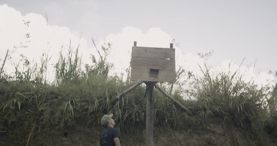 A boy shoots a basketball and scores at a hoop on a dirt road
