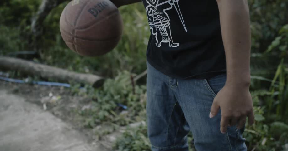 Man wearing a hat bounces a basketball on a sidewalk as others watch