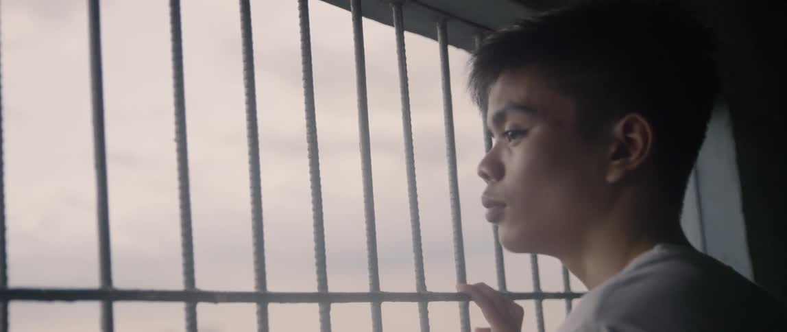 A man holds the bars on the window looking out