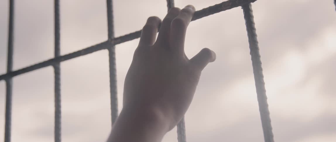 Fingers cling to the bars of a gate