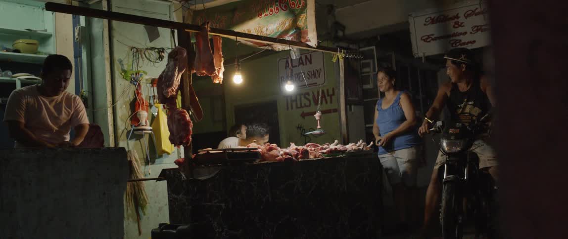 A man on motorbike is parked next to a butcher shop counter as meat is chopped