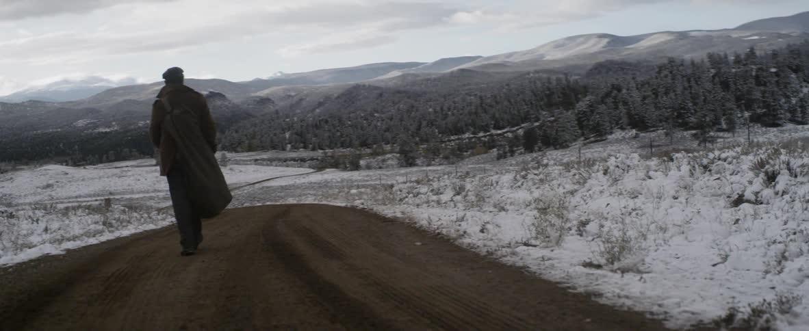 Man walking down a trail with a vast snow fields and mountains ahead