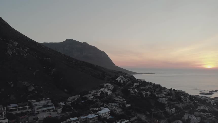 Homes on a sloping hill leading to the ocean at sunset