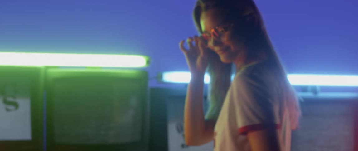 A woman is being flirtatious as she stands in front flashing televisions