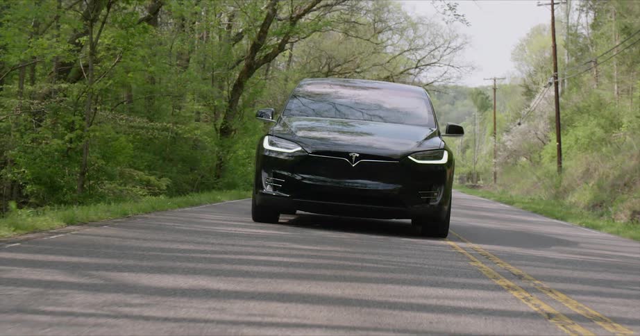 A tesla vehicle is driving on a country road in daylight