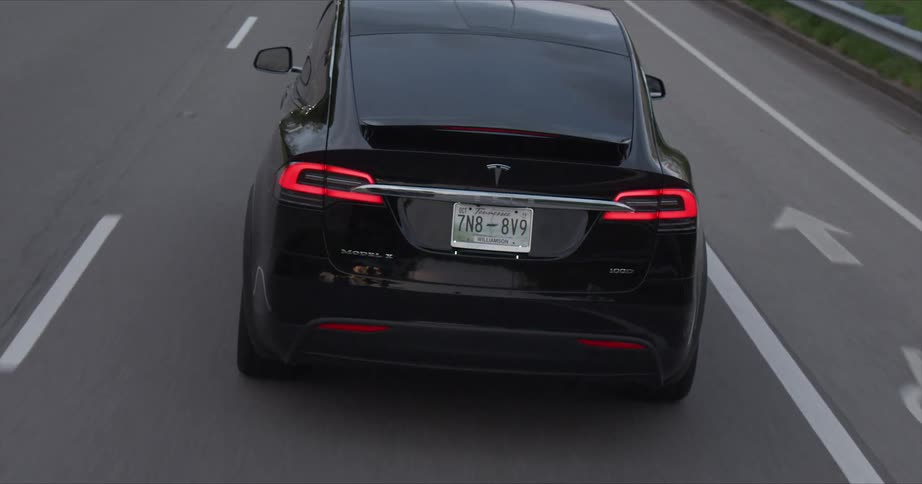 A tesla vehicle is driving on a highway at dusk