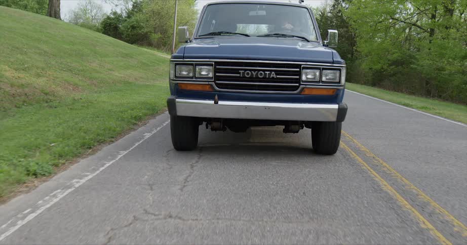 A blue pickup truck rides on a rural road