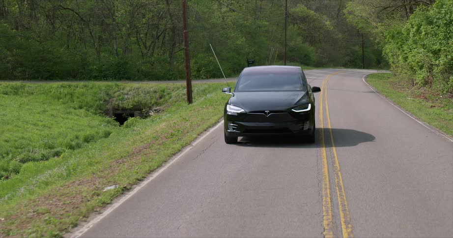 The car is driving on the road near the forest