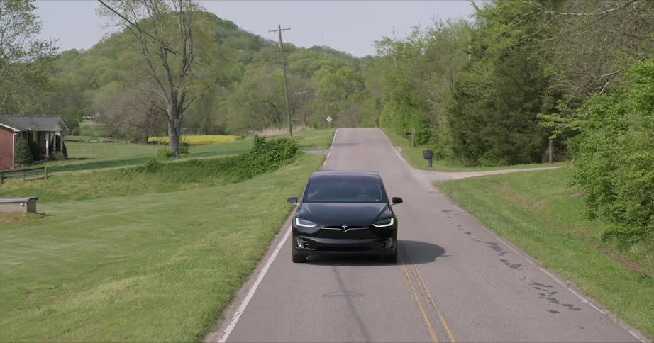 Black car travels down the road past the green grass