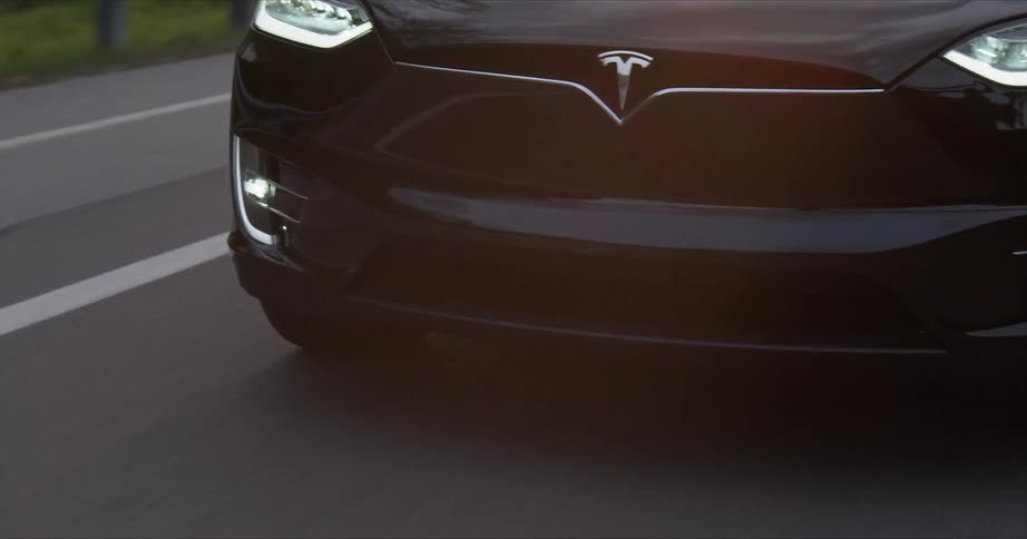 A tesla vehicle is driving on a country road in daylight