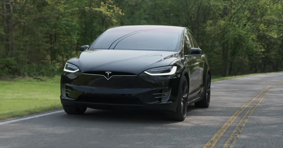 A tesla vehicle is driving on a country road in daylight