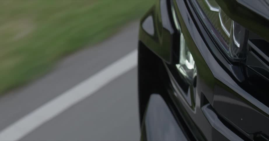 Black vehicle travels down a road on a clear day