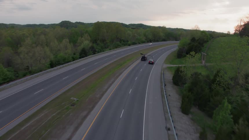 Vehicles drive down a highway next to the trees under a cloudy sky