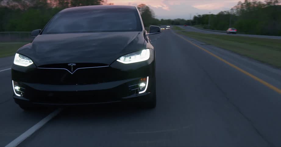 A tesla vehicle is driving on a highway at dusk