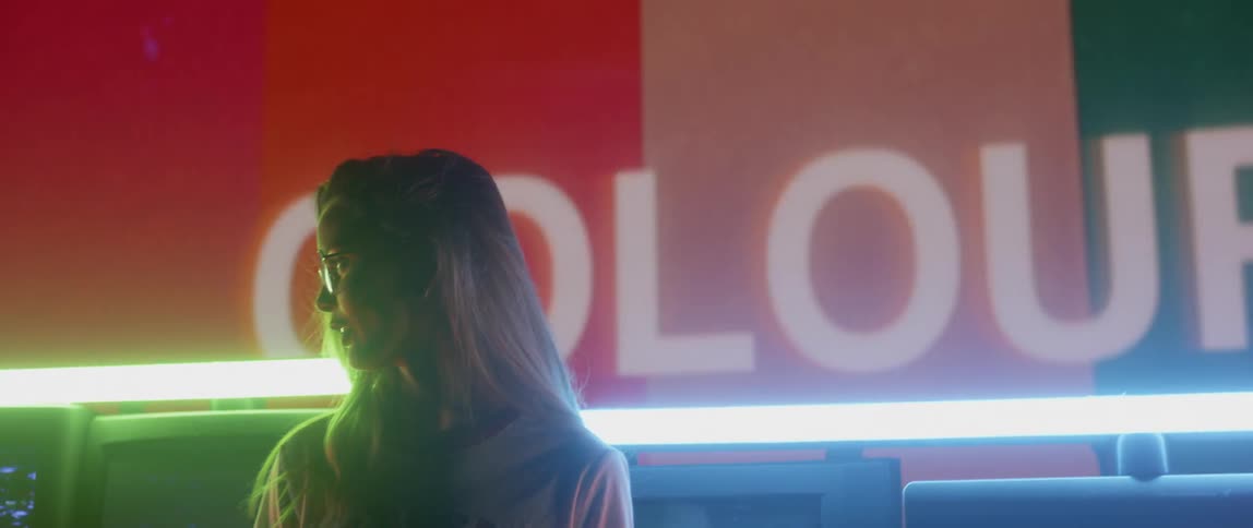 A woman looks to her side smiling in front of the flashing televisions
