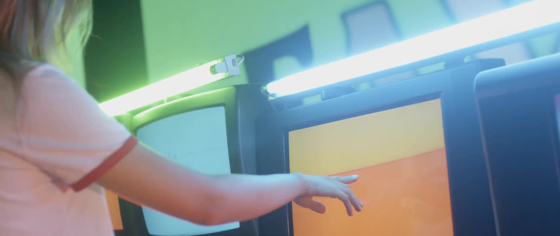 A woman walks up and touches a flashing television