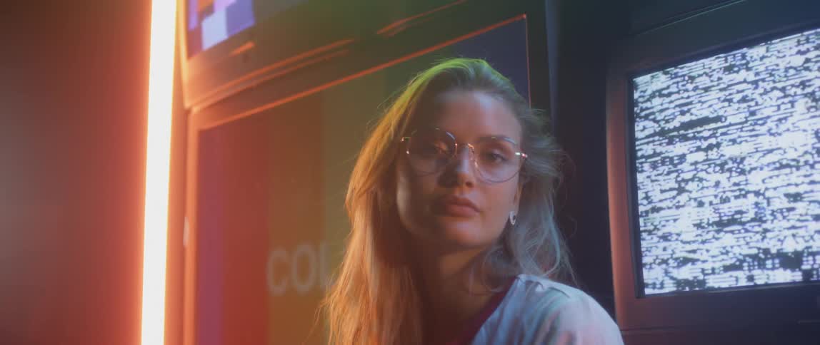 A woman stands in front of flickering television screens