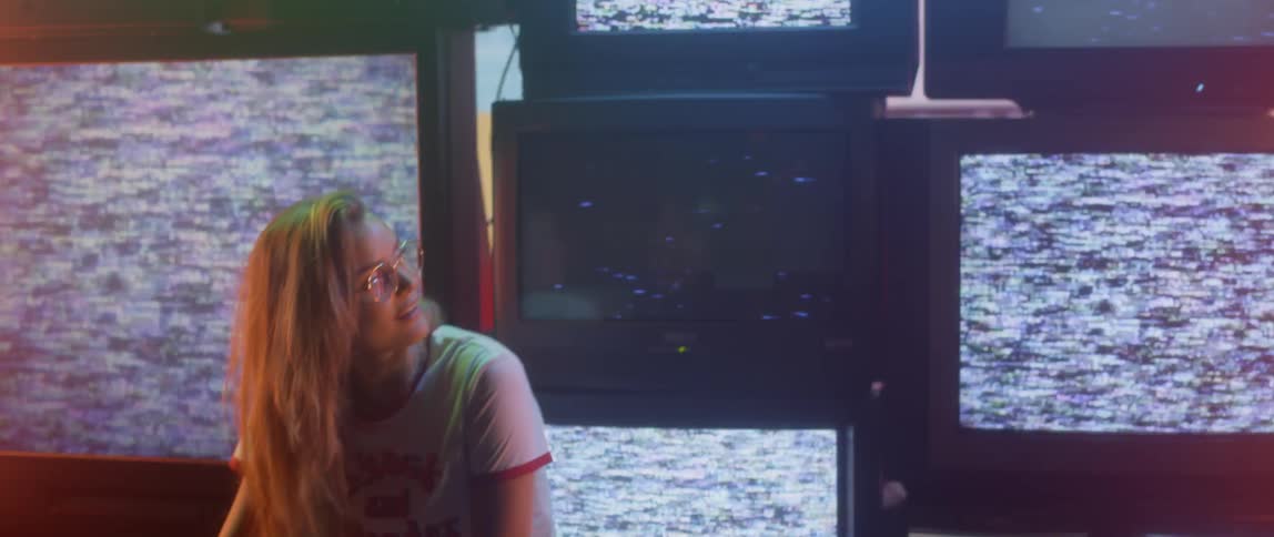 A woman is sitting in front of a bank of televisions flashing images