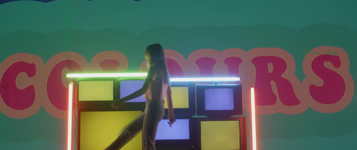A woman dances in front of televisions strobing vibrant colors