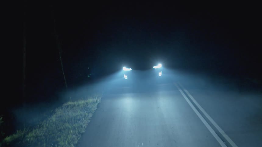 Headlights from a vehicle shine on a road at night