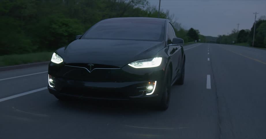 A tesla vehicle is driving on a highway at dusk