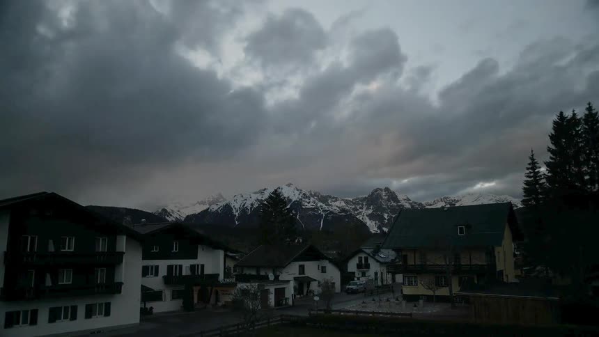 Clouds roll over houses and snowy mountains