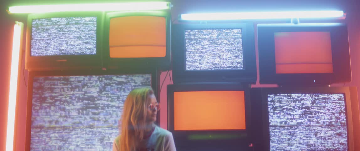 Woman stands in front of many screens flashing images and lights