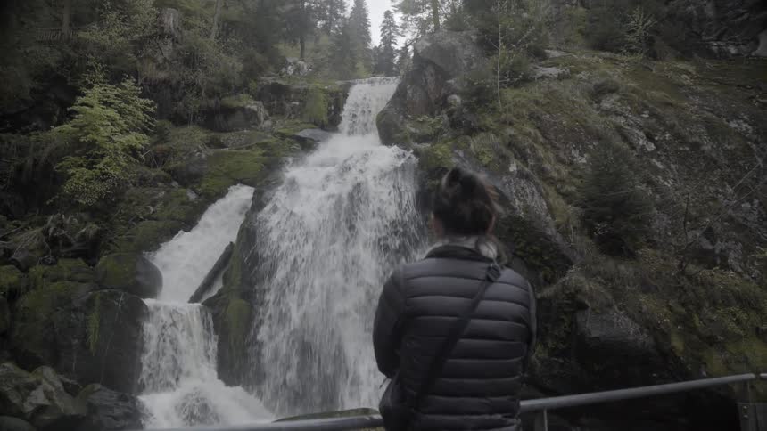 Woman is standing by railing and looking at waterfall