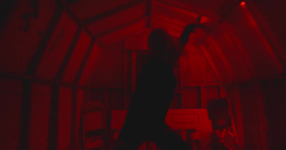 A woman dances in a shack illuminated by red light