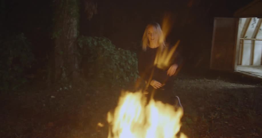 Woman dances by a large fire outside at night